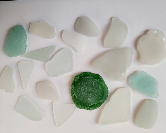 A close-up shot of a hand sifting through sea glass of various colors on the beach, catching the sunlight, showing texture and the variety of colors.