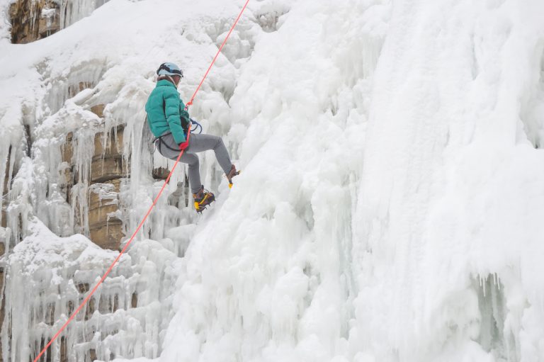An action shot of a canyoner rappelling down a frozen waterfall with ice formations framing the scene.