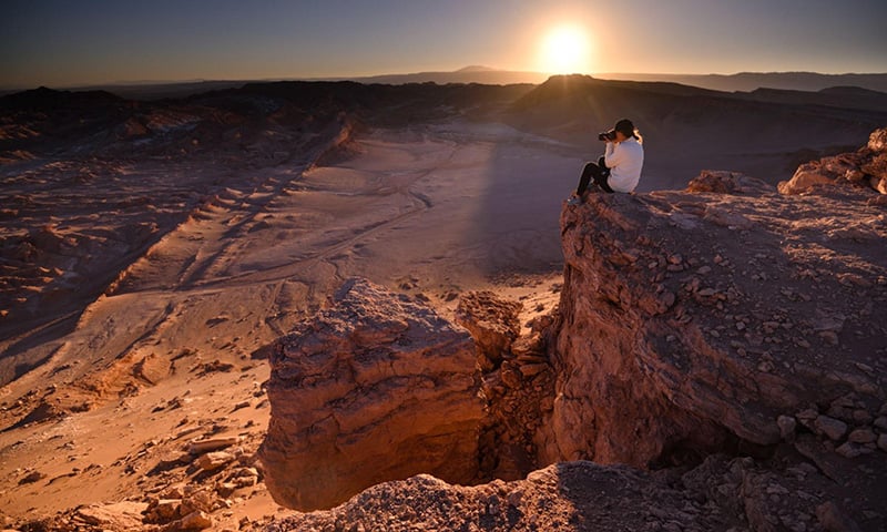 Eliza meditating in the desert, surrounded by rocks and sand, with a serene expression