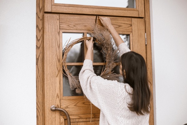 A woman decorates a front door with foraged materials