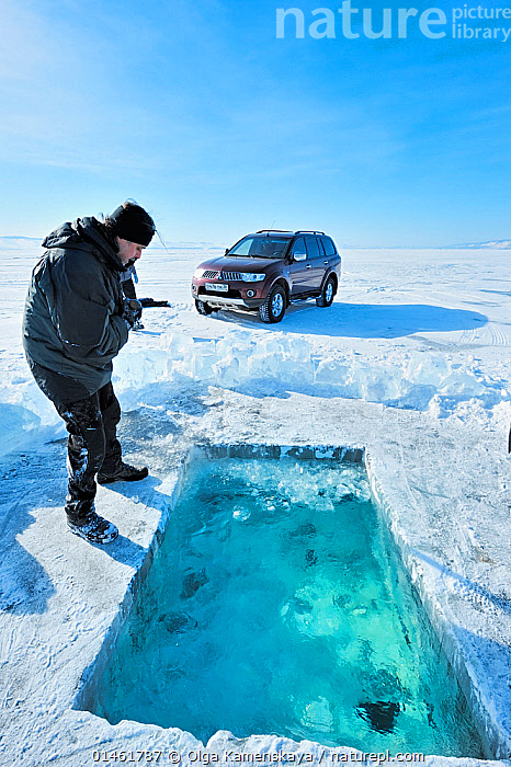 Ice divers emerging from a hole cut in the thick, frozen ice of Lake Baikal. The surrounding ice formations create an otherworldly scene, emphasizing the remoteness and beauty.
