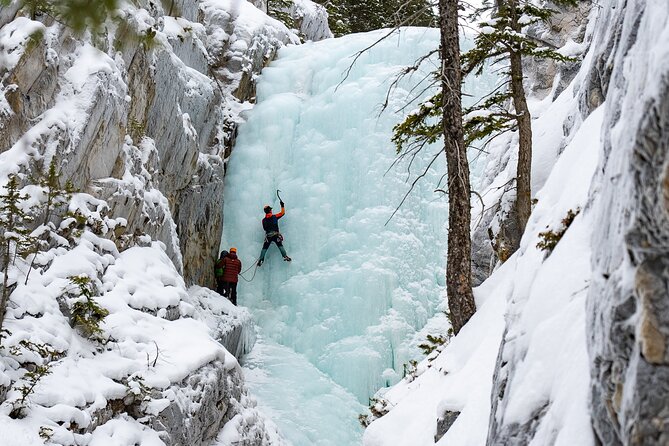 A climber ascending a frozen waterfall at Johnston Canyon, with turquoise ice shimmering in the sunlight.