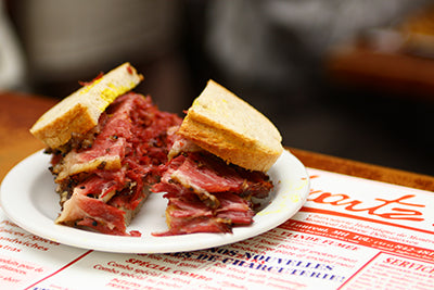 A classic Montreal smoked meat sandwich from Schwartz's Deli, showcasing the generous portion of thinly sliced meat piled high on rye bread. The alt text highlights Schwartz's legendary status and emphasizes the unique curing process of their smoked meat.