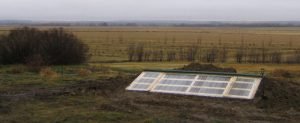 A cross-section of a cold frame illustrates the principle of solar heat trapping, showcasing how sunlight enters, warms the soil and air, and is retained within the enclosed structure.