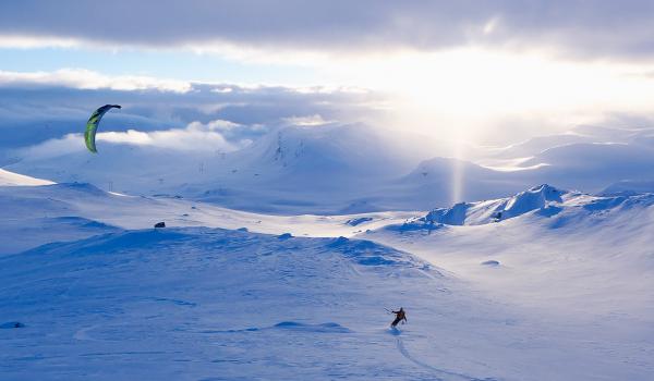 A snowkiter soaring across a vast, white landscape in Iceland under a dramatic sky filled with swirling clouds, capturing the sense of movement and the raw beauty of the country.