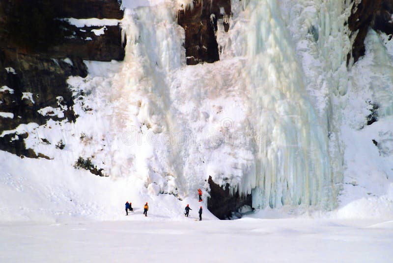 Ice climber ascending a frozen waterfall with ice spraying around them.