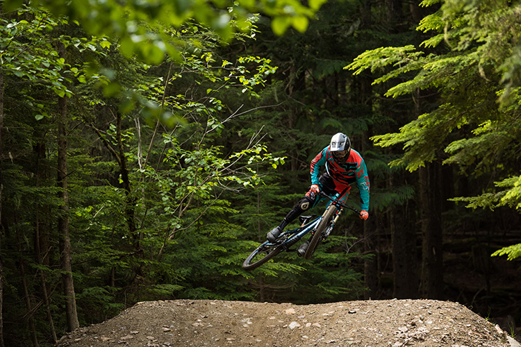 A mountain biker catches air on a large jump on the A-Line trail at Whistler Bike Park, showcasing the height and dynamism of the jump as well as the skill of the rider.