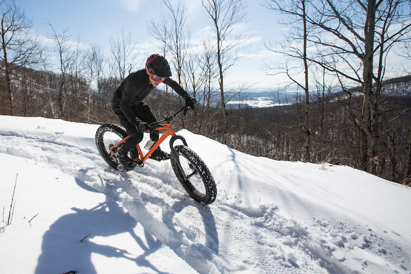A lone fat biker traverses a snowy trail in the Eastern Townships, surrounded by snow-covered trees. This image highlights the vastness of the landscape and the individual's pursuit of fat biking adventure.