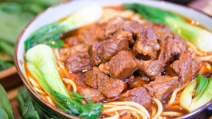 A close-up shot of a bowl of beef noodle soup, highlighting the broth, noodles, beef, and garnishes.
