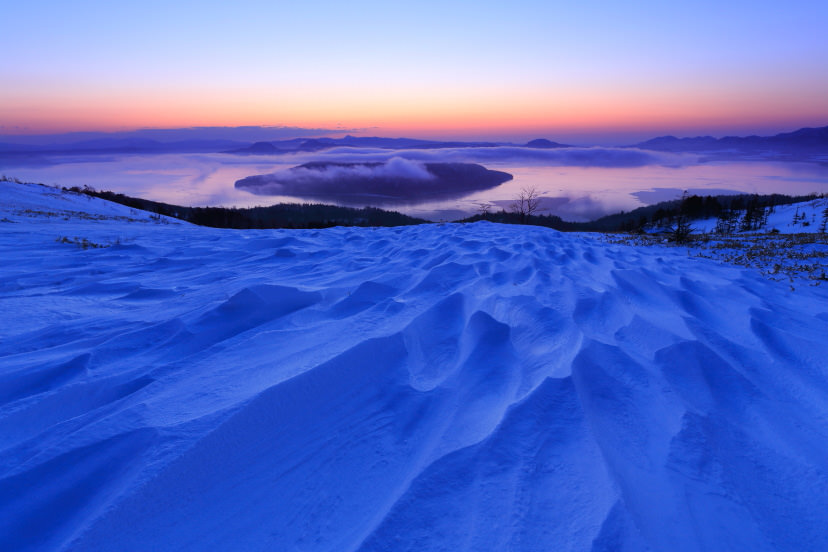 A snowy landscape with a person in bright clothing walking on ice, showcasing the vastness and beauty of drift ice walking in Utoro.