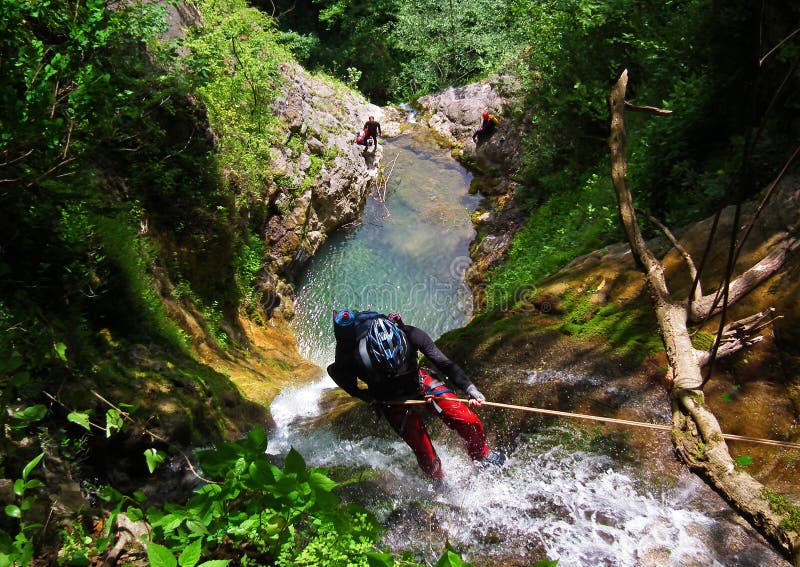 A canyoneer rappels down a waterfall in the Apuseni Mountains, surrounded by moss-covered limestone cliffs, showcasing the exhilarating nature of the adventure.