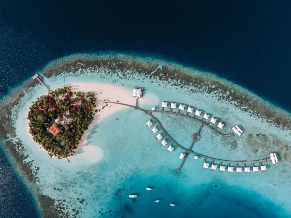Exterior shot of an overwater bungalow with a wooden deck, chairs, and clear water