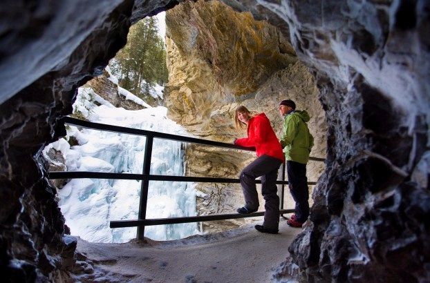 A frozen waterfall inside Johnston Canyon. The ice is blue and translucent, and icicles hang from the canyon walls.