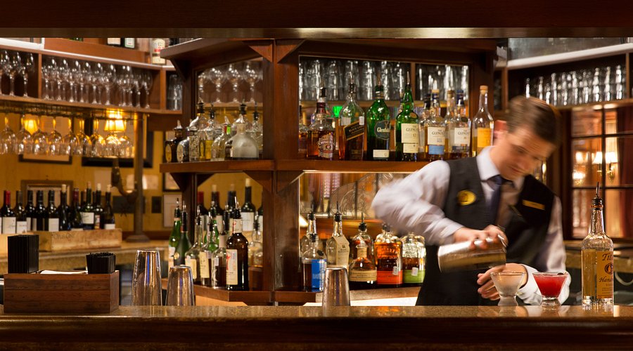 The Driskill Bar, showcasing its dark wood, elegant lighting, and patrons enjoying drinks