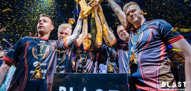 Aleksib holding the trophy above his head while his teammates cheer