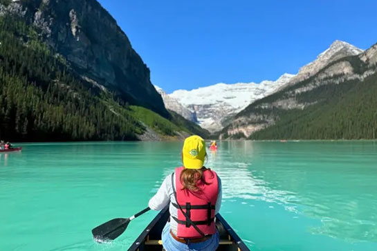 A canoe glides across the turquoise waters of Lake Louise, reflecting the surrounding mountains
