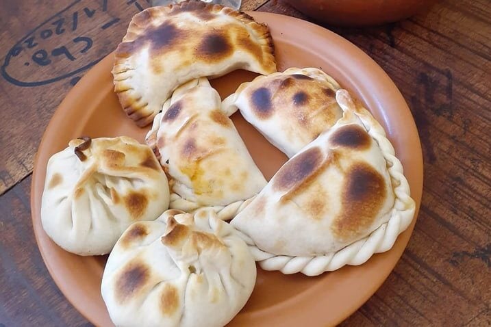 A colorful display of various regional empanadas, showcasing their different shapes, fillings, and golden-brown crusts. The natural light highlights the textures and vibrancy of each empanada.