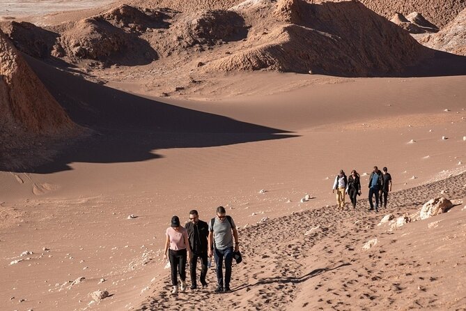 The Hand of the Desert, a large sculpture emerging from the sand in the Atacama Desert, Chile. The sun casts long shadows, enhancing the sculpture's size and surreal presence.