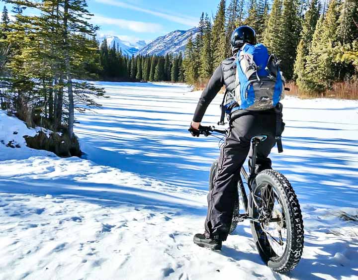 Fat biker riding along the snow-covered Bow River Trail with the mountains in the background.