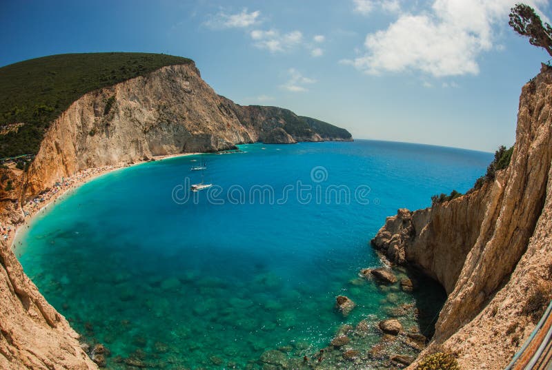 A stunning panoramic view of a secluded beach with turquoise water, white sand, and lush green hills in the background.