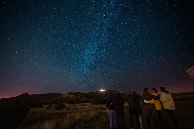 A breathtaking shot of the Milky Way arcing over telescopes, with travellers taking astrophotography shots.