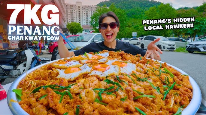 A chef stir-frying Char Kway Teow in a wok with flames bursting upwards