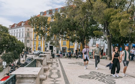 A photo of Lisbon at dusk, showing the rooftops of Alfama, with a warm, colorful sunset in the background.