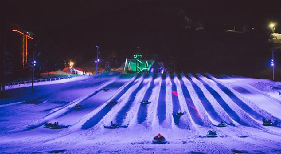 Families enjoying night snow tubing at Mount Hood, Oregon, with colorful LED lights illuminating the slopes. The alt text focuses on the festive atmosphere and the joy of the participants, highlighting the family-friendly aspect of the activity.