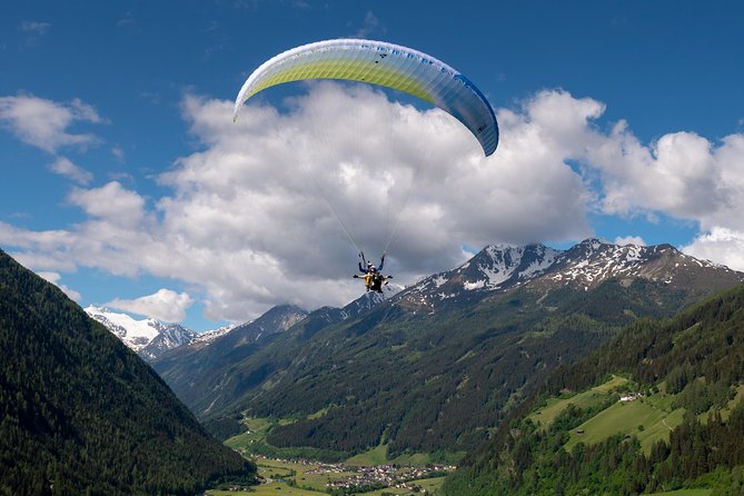 A paraglider silhouetted against a blue sky over a quaint Austrian village