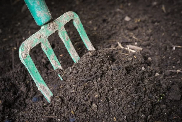 Someone turning compost inside a compost bin
