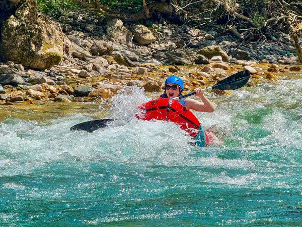 A person packrafting on a turquoise river in a mountain valley, with trees and rocks along the banks.