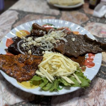 A vibrant tlayuda loaded with black beans, quesillo, lettuce, tomato, avocado, and salsa, displayed on a traditional Oaxacan plate.