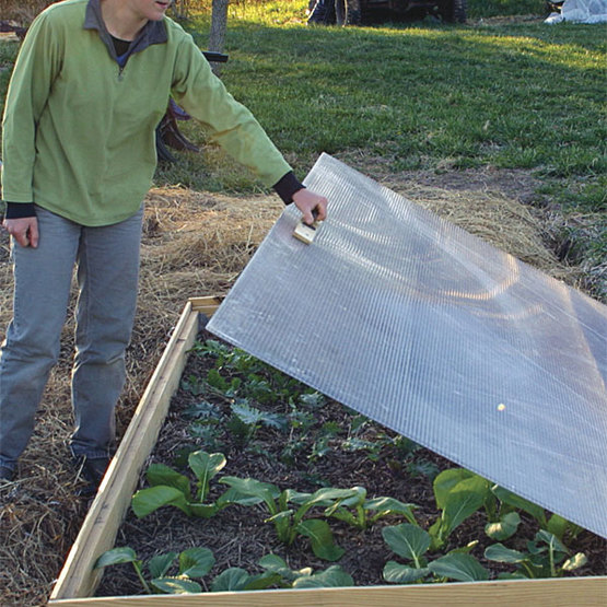 A close-up of a cold frame ventilation system, showing a hinged vent on the side.