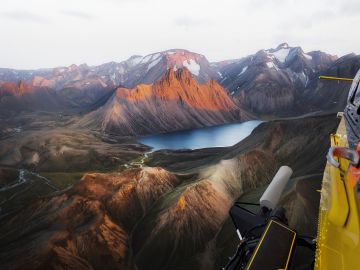 A hiker standing on the Fimmvörðuháls Pass, surrounded by black lava fields, green moss, and a distant glacier.