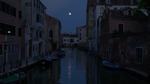 A quiet canal scene in Venice at night, illuminated by moonlight, with reflections shimmering on the water and a glimpse of a bridge in the background, evoking a sense of tranquility and discovery.