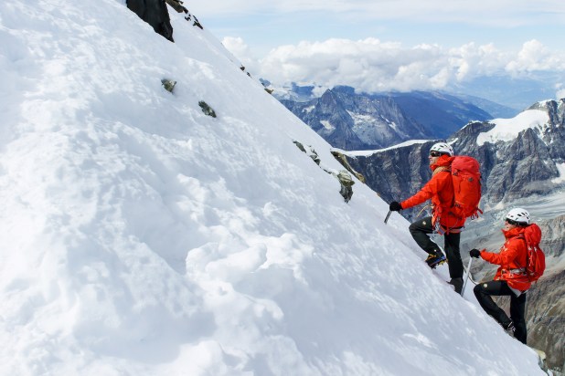 An ice climber ascending a frozen waterfall in Zermatt, with the Matterhorn majestically towering in the background.