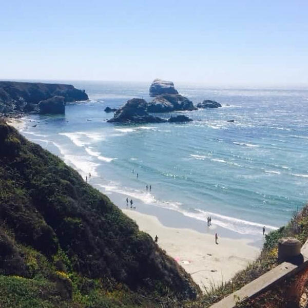 Lisa and Lily setting up a tent at Kirk Creek Campground, with the ocean visible in the background. Lily is holding a tent peg while Lisa works on securing a pole.