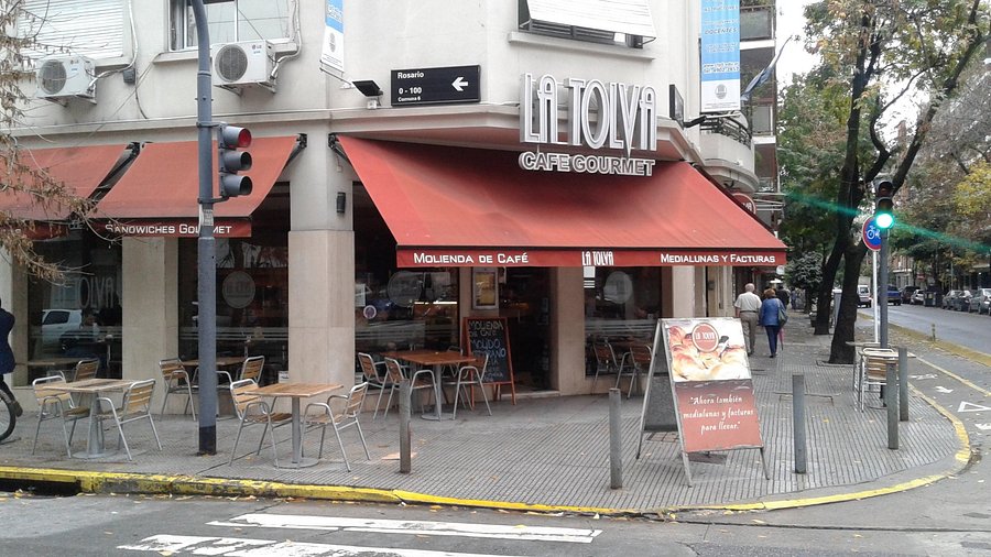 A glass of Fernet con Coca with ice, garnished with a lime wedge, set against the backdrop of a bustling sidewalk cafe in Palermo. The shallow depth of field focuses on the drink while blurring the cafe scene.