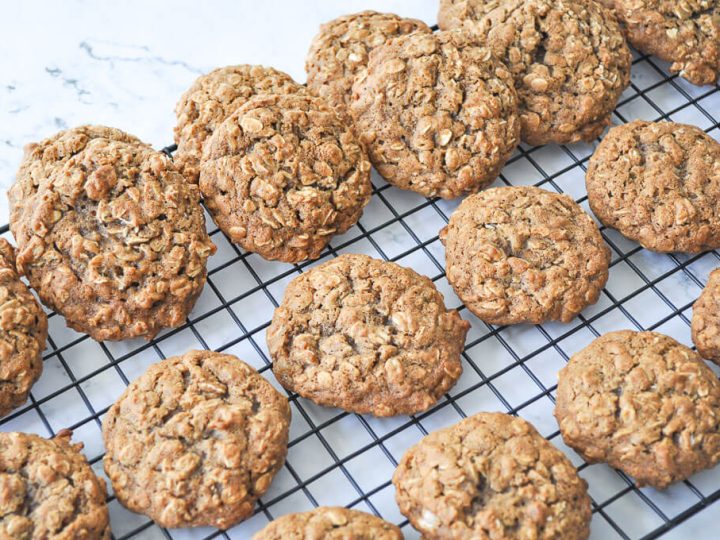 A wide-angle shot of Apple Butter Sweet Potato Biscuits with Candied Sage cooling on a weathered wooden wire rack, beside apple butter and a spread biscuit.