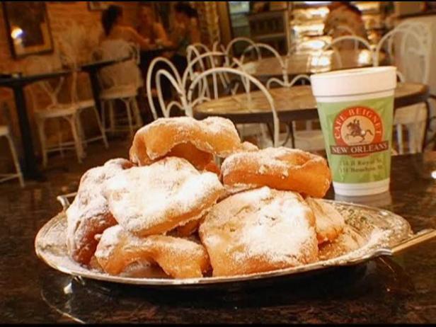 A close-up shot of beignets covered in powdered sugar, alongside a cup of cafe au lait at Cafe Du Monde.