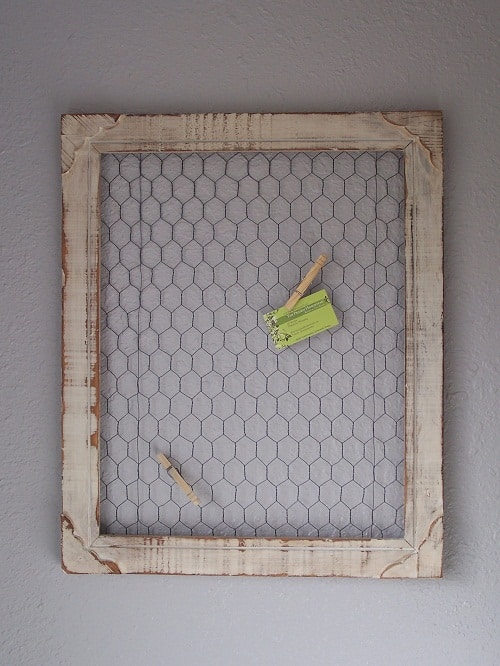 A section of chicken wire attached to a farmhouse kitchen wall, with sprigs of rosemary and thyme clipped on using wooden clothespins.