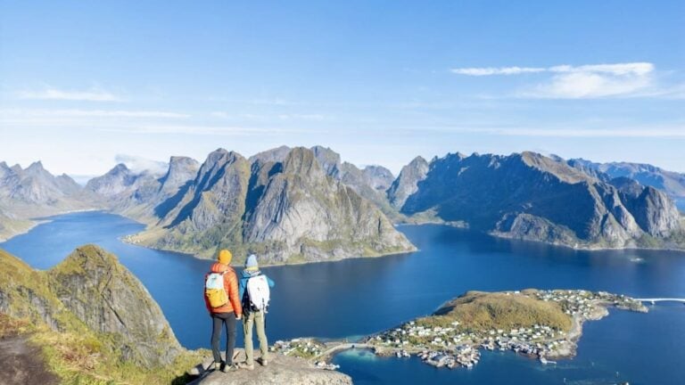 A panoramic photograph showing a skier descending towards the coastline with the ocean in the background, taken on a clear day with strong sunlight