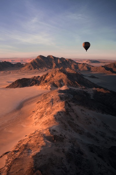 A panoramic shot of Sossusvlei from a hot air balloon at sunrise, capturing the shadows stretching across the red dunes and the vibrant colors of the rising sun.