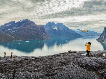 An underwater photographer captures images beneath the ice. Sunlight filters through the ice hole, illuminating the frigid water and marine life.