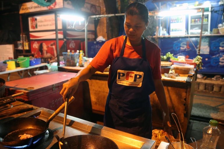 A candid photo of the Pad Thai street vendor, capturing a genuine smile and the interaction with the traveler. The photo uses a warm color temperature to emphasize the street food atmosphere.